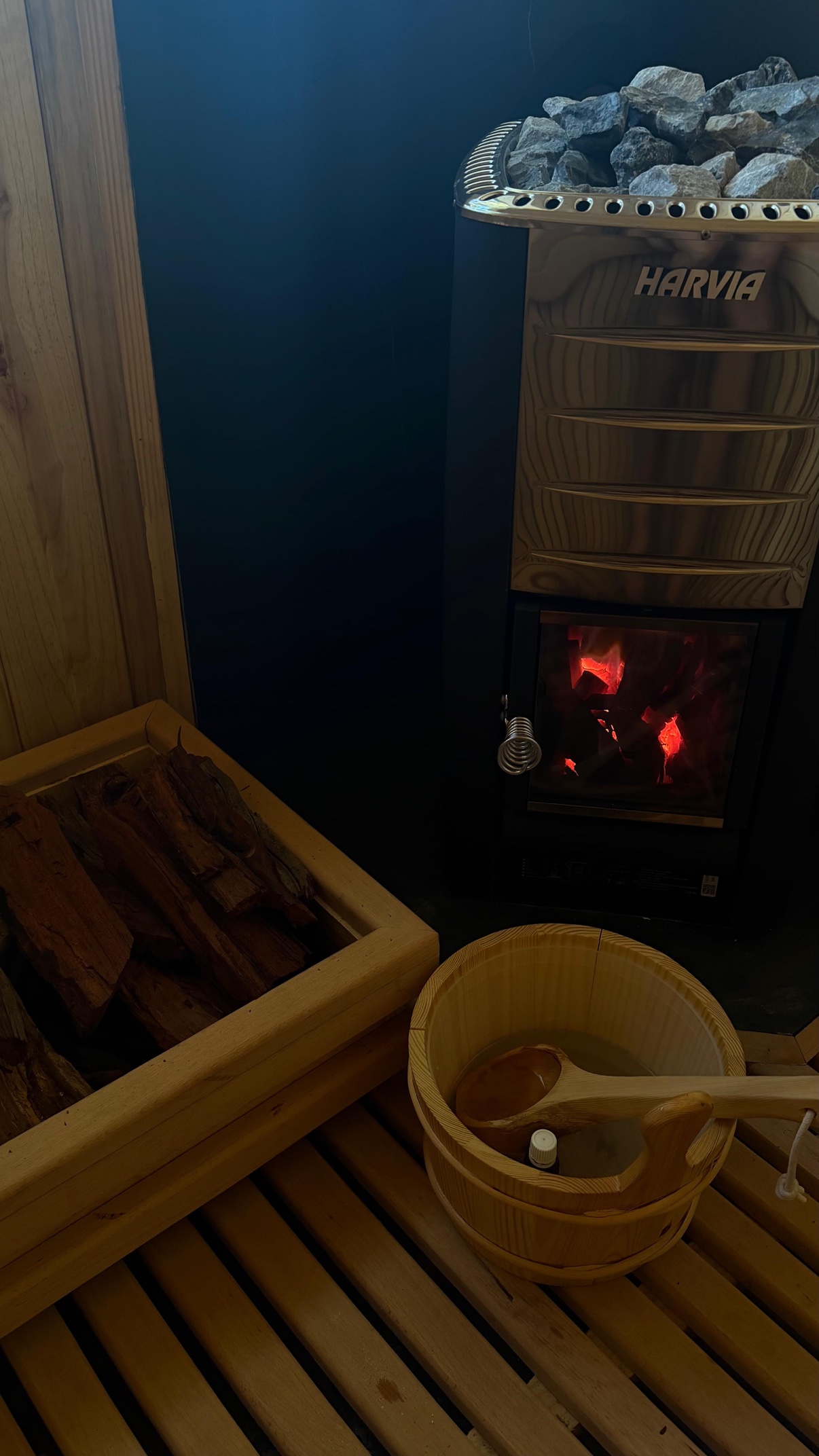 Wood-fired sauna interior with Harvia stove, glowing coals, and wooden bucket at Zania Farm